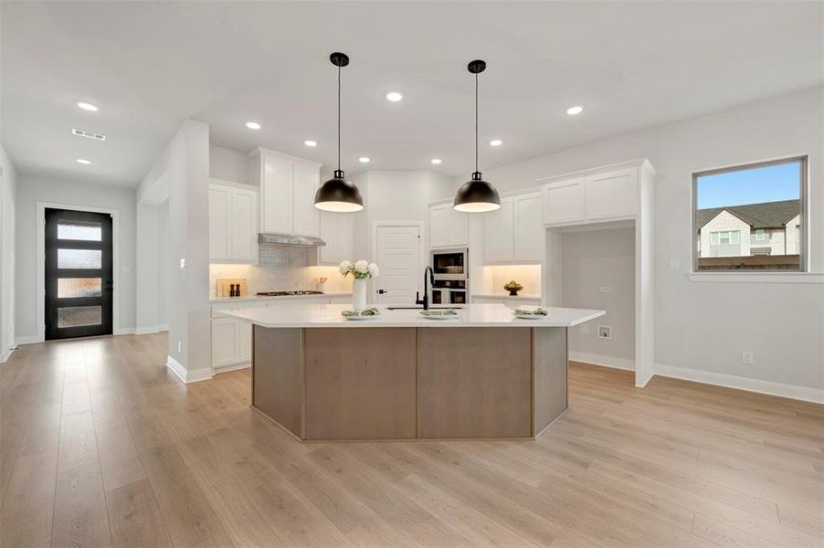 Kitchen featuring healthy amount of natural light, a kitchen island with sink, light wood finished floors, and two tone cabinetry