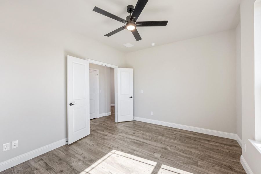 Empty bedroom with wood-look floors, ceiling fan, and two white doors leading to closet and hallway Empty bedroom with wood-look floors, ceiling fan, and two white doors leading to closet and hallway