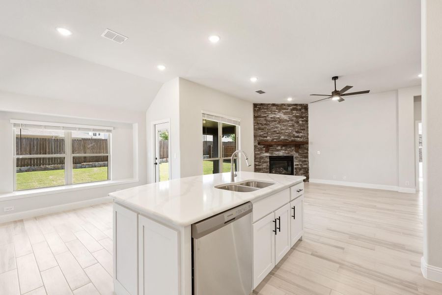 Kitchen island with white cabinets and sink open to living room with stone fireplace and ceiling fan Kitchen island with white cabinets and sink open to living room with stone fireplace and ceiling fan