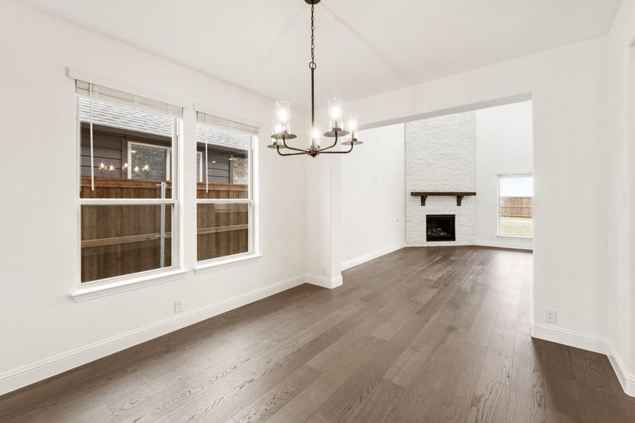 Open dining area with chandelier and dark hardwood floors, opening to living room with stone fireplace