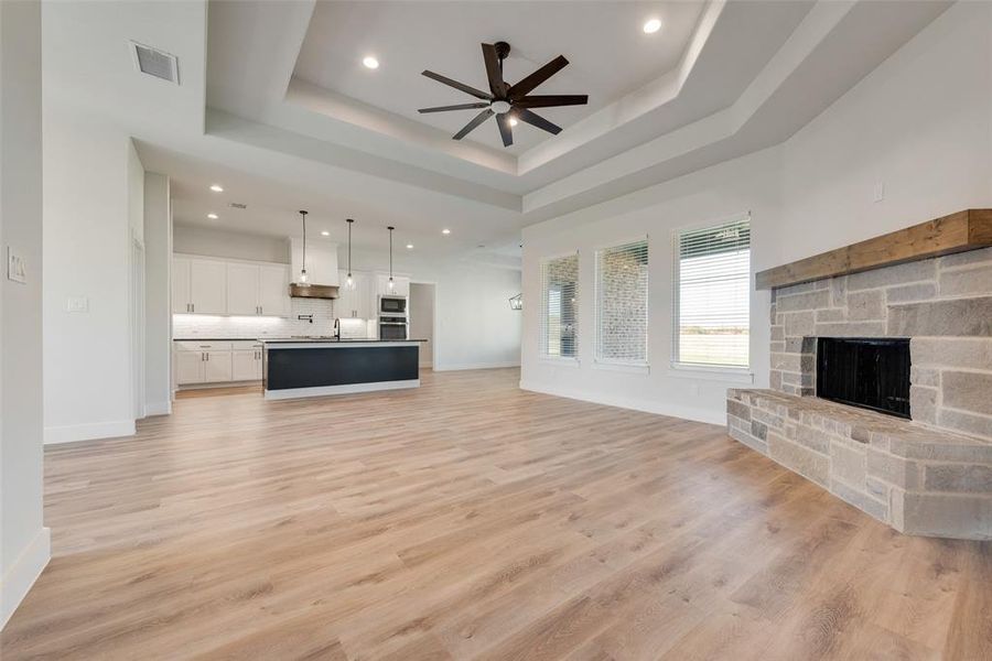 Unfurnished living room featuring a stone fireplace, a raised ceiling, sink, light hardwood / wood-style flooring, and ceiling fan