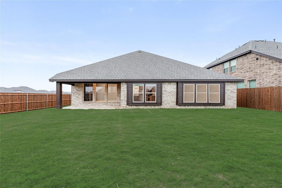 Rear view of single-story brick home with large backyard, covered patio, and wood privacy fence