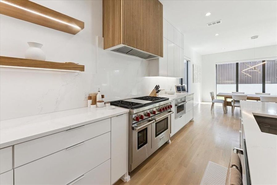 Kitchen with modern cabinets, white cabinetry, hanging light fixtures, range with two ovens, and premium range hood