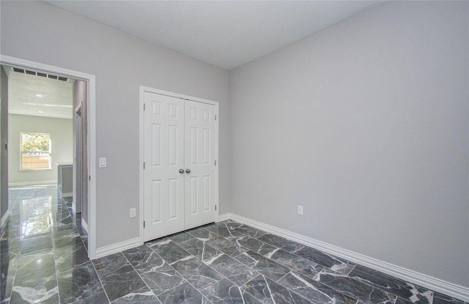 This room features sleek gray walls and polished marble flooring. It includes a double-door closet and opens into a bright, spacious area with large windows, offering ample natural light.