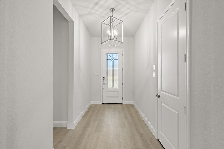 Elegant doorway showcasing light hardwood or wood-style floors, complemented by a stylish chandelier that adds a touch of sophistication to the entryway.