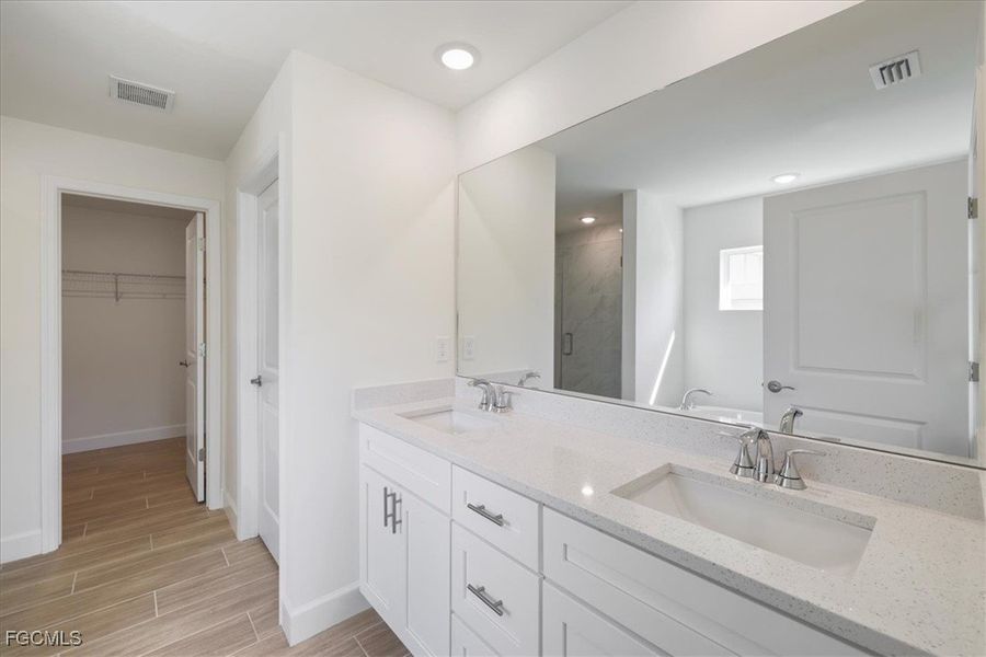 Full bathroom featuring a spacious closet, double vanity, a marble finish shower, wood tiled floors, and a bath
