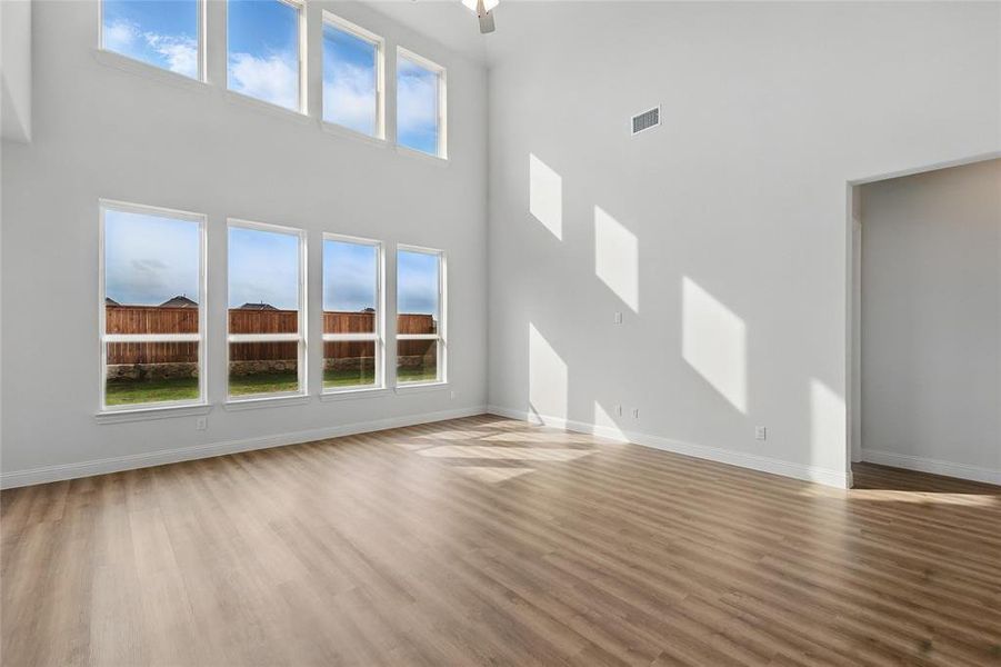Unfurnished living room with visible vents, a high ceiling, and wood finished floors Unfurnished living room with visible vents, a high ceiling, and wood finished floors