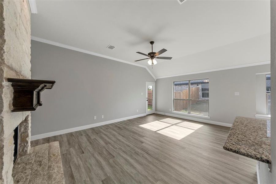 Unfurnished living room featuring lofted ceiling, a stone fireplace, crown molding, light hardwood / wood-style flooring, and ceiling fan