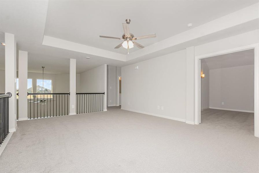 Spare room with a tray ceiling, light colored carpet, and a ceiling fan