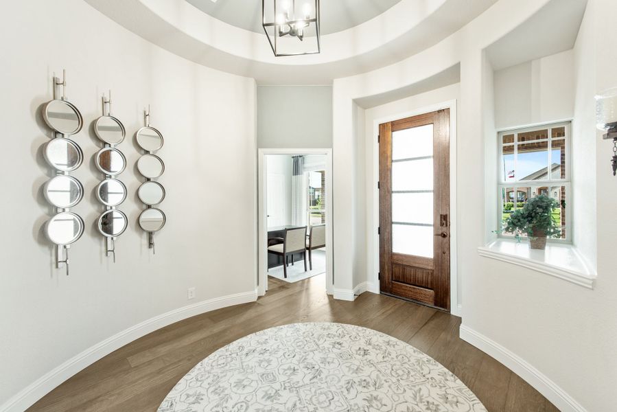 Round foyer with tray ceiling, chandelier, wood front door with glass panel, and hardwood floors