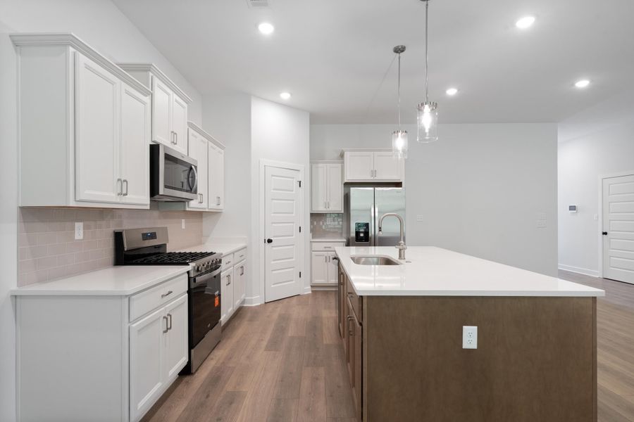 Kitchen featuring white cabinetry, stainless steel appliances, wood-finish flooring, a central island with a sink, and pendant lighting