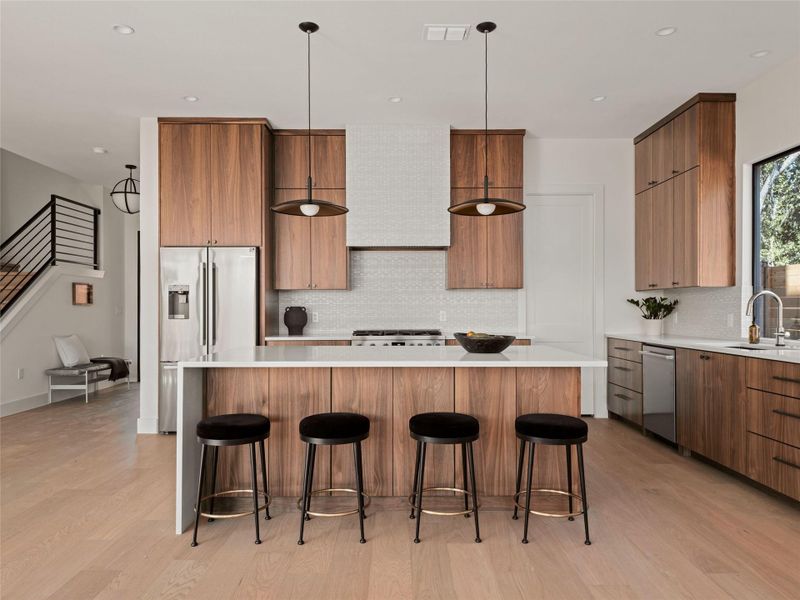 Kitchen featuring tasteful backsplash, light wood finished floors, hanging light fixtures, stainless steel appliances, and modern cabinets