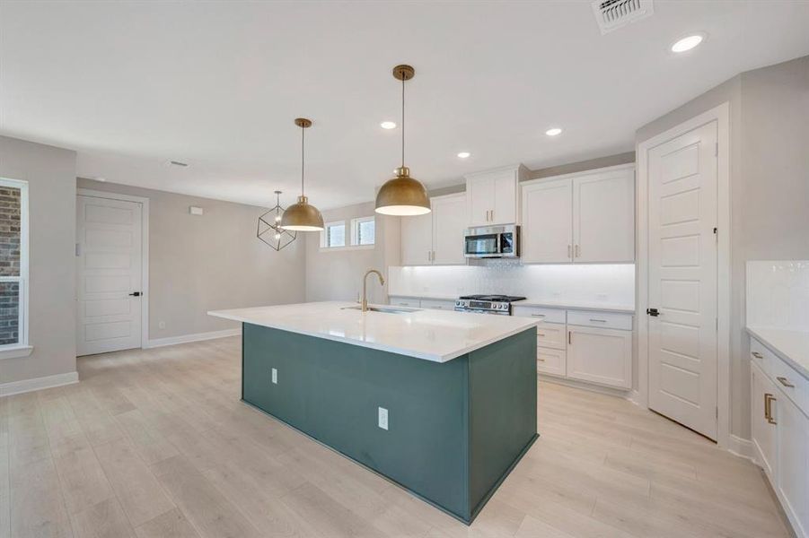 Two tone kitchen with an island with sink, pendant lighting, light wood-style flooring, stainless steel appliances, and dual tone cabinets