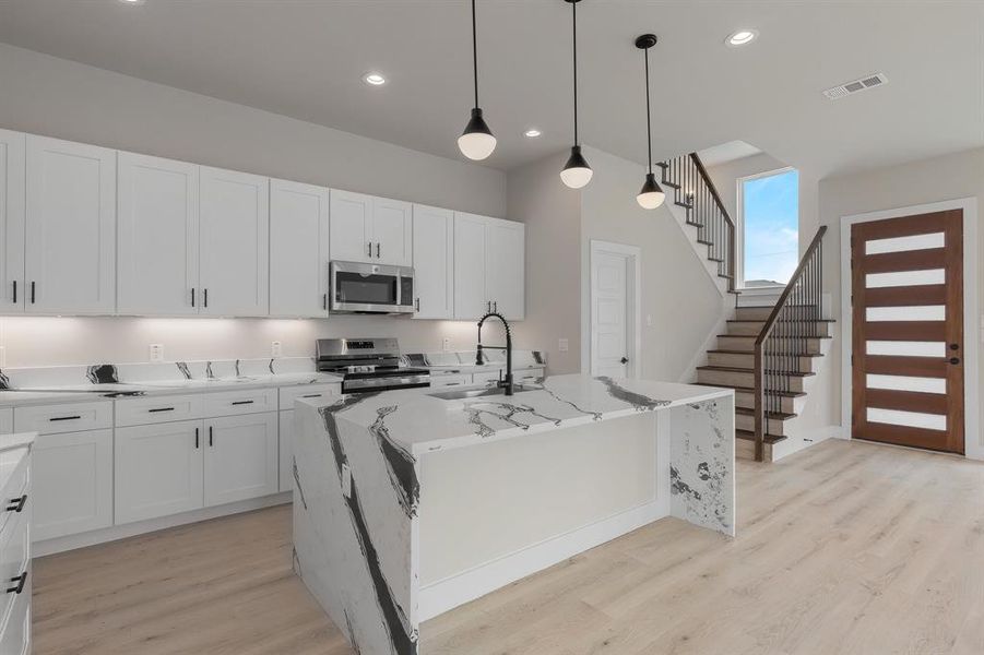 Kitchen with appliances with stainless steel finishes, a sink, light wood-style floors, an island with sink, and light stone countertops
