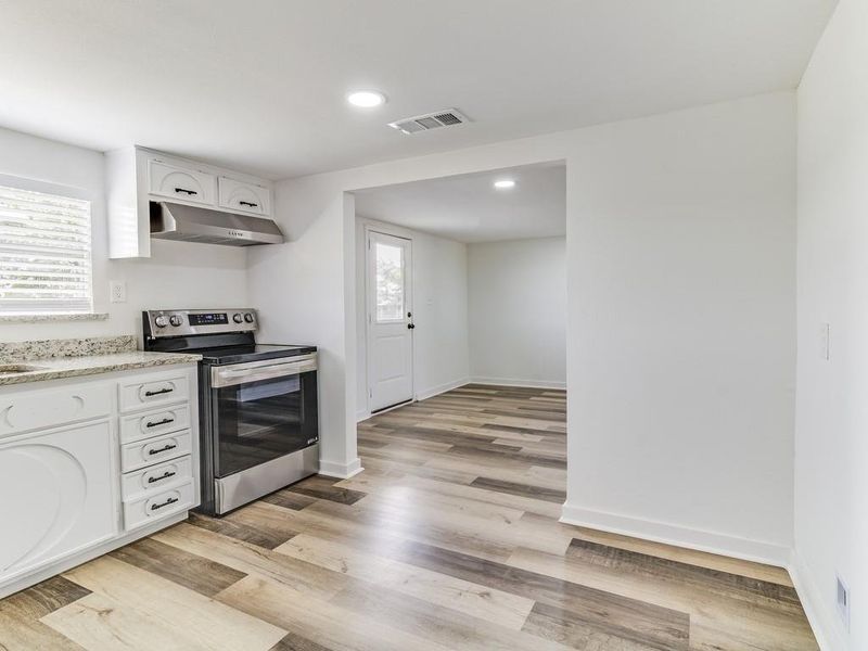 Kitchen with under cabinet range hood, stainless steel range with electric cooktop, light wood-style flooring, white cabinets, and recessed lighting Kitchen with under cabinet range hood, stainless steel range with electric cooktop, light wood-style flooring, white cabinets, and recessed lighting
