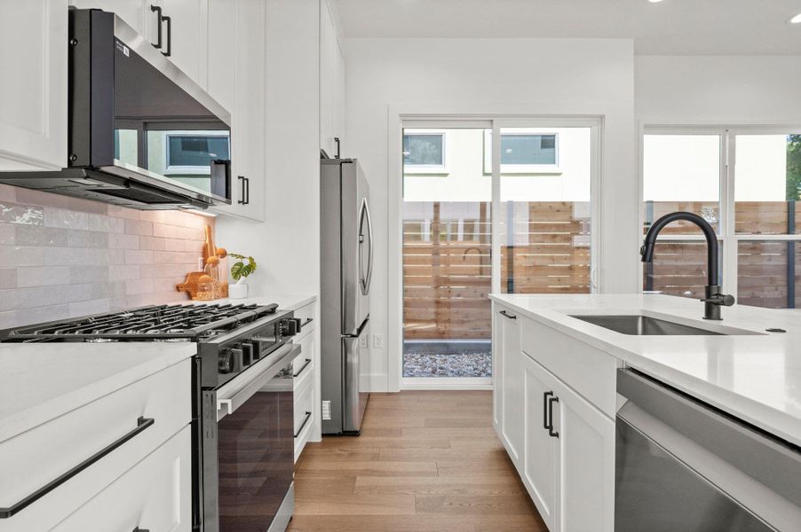 Kitchen with white cabinetry, appliances with stainless steel finishes, light wood-type flooring, light stone counters, and backsplash Kitchen with white cabinetry, appliances with stainless steel finishes, light wood-type flooring, light stone counters, and backsplash