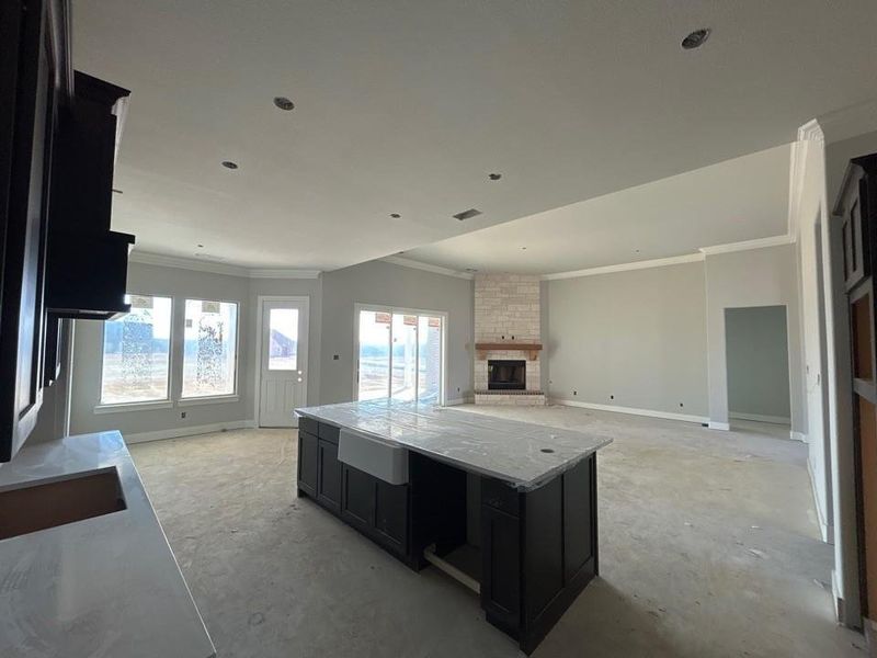 Kitchen with dark cabinetry, a fireplace, ornamental molding, a center island, and light stone counters