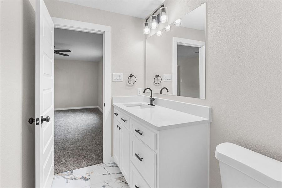 Primary bathroom featuring vanity, light marble finish floors, light colored carpet, and ceiling fan