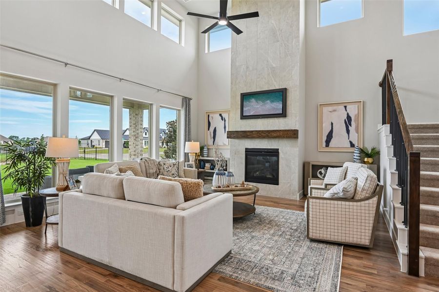 Living room with two-story ceiling, stone fireplace, hardwood floors, and large windows with backyard view Living room with two-story ceiling, stone fireplace, hardwood floors, and large windows with backyard view