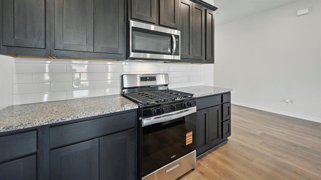 Kitchen with appliances with stainless steel finishes, light stone countertops, decorative backsplash, and light wood-type flooring