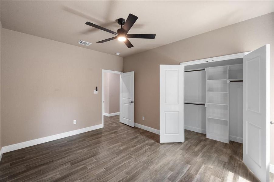 Room featuring wood-finish tile flooring, neutral wall paint, and a modern black ceiling fan, with large custom closet