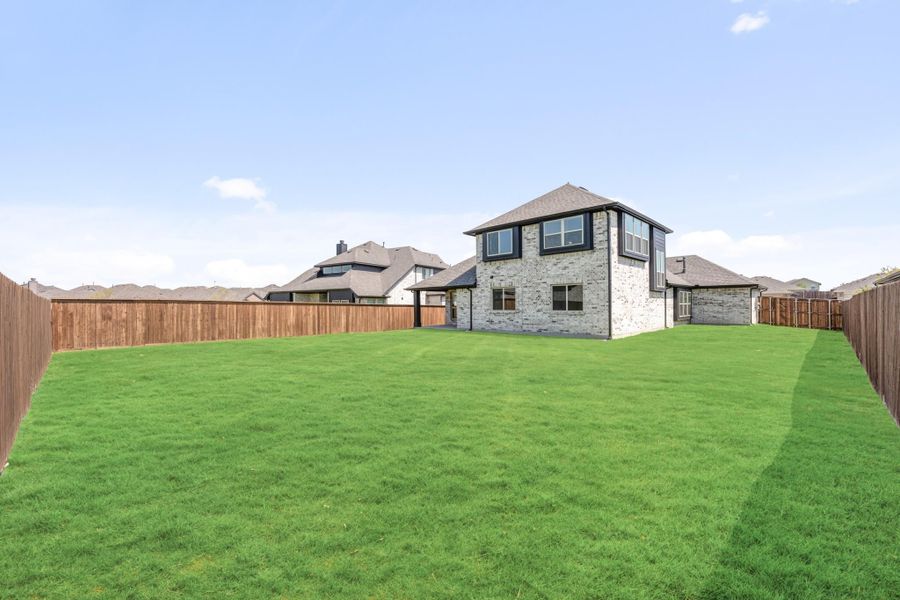 Two-story brick home with large fenced backyard and green lawn viewed from rear Two-story brick home with large fenced backyard and green lawn viewed from rear