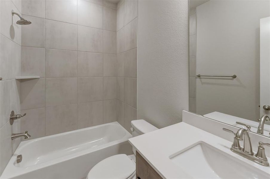 Bathroom featuring a white bathtub with a tiled surround, a toilet, a vanity with a white countertop, an undermount sink, and brushed nickel fixtures