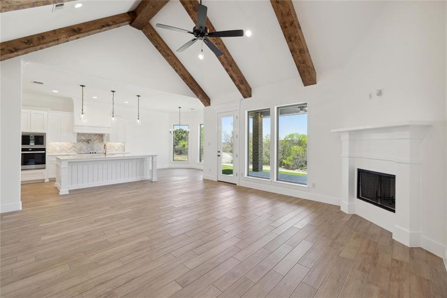 Unfurnished living room featuring light wood-type flooring, a wealth of natural light, and beam ceiling