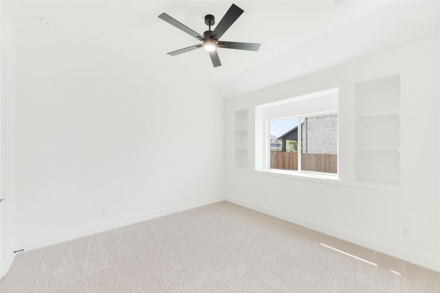 Empty bedroom with vaulted ceiling, ceiling fan, built-in shelves, and carpet flooring