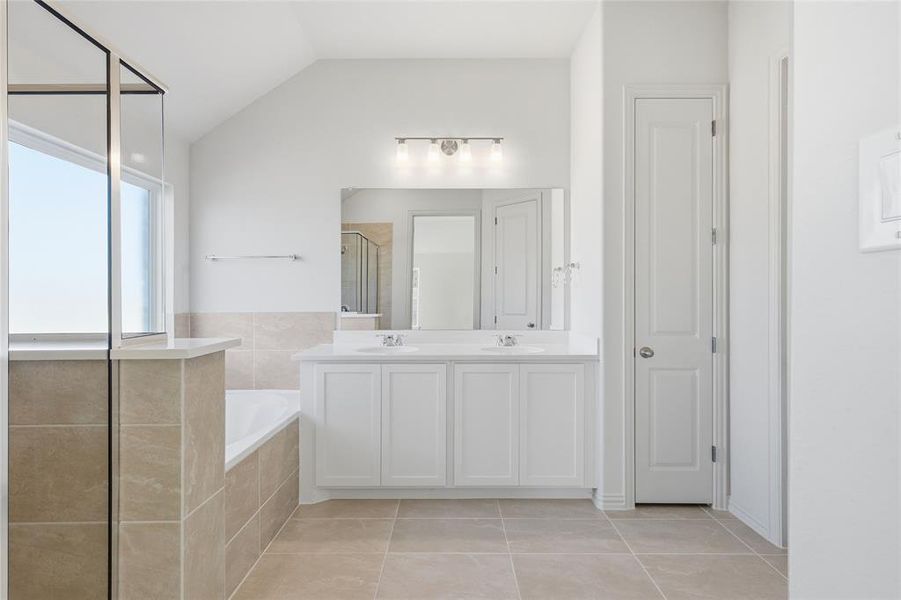 Bathroom featuring a stall shower, double vanity, lofted ceiling, light tile patterned flooring, and a garden tub Bathroom featuring a stall shower, double vanity, lofted ceiling, light tile patterned flooring, and a garden tub
