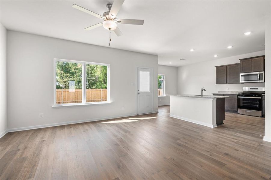 Kitchen with a center island with sink, appliances with stainless steel finishes, dark brown cabinetry, dark wood-style flooring, and open floor plan