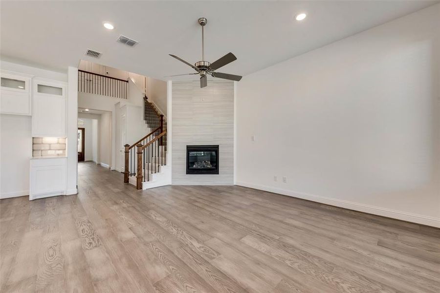 Unfurnished living room with ceiling fan, light wood-type flooring, and a tile fireplace