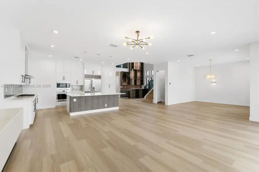 Open-concept area featuring wood-finish flooring, a kitchen island with stone countertop, white cabinetry with contrast base, modern chandelier lighting, and recessed ceiling lights