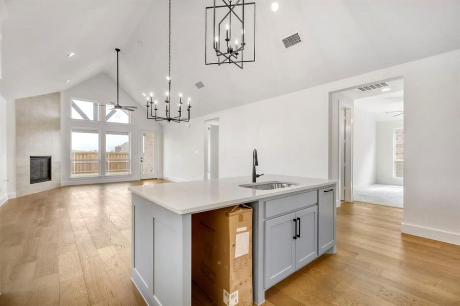 Kitchen featuring a ceiling fan, a high ceiling, a kitchen island with sink, a fireplace, and hanging lights