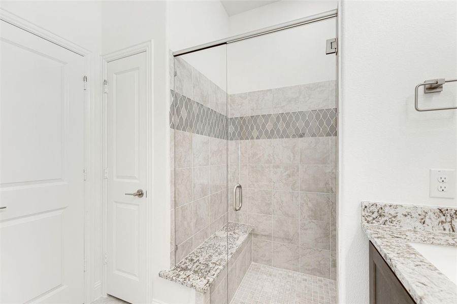 Walk-in shower with glass door, gray tile walls, decorative border, and built-in bench seat Walk-in shower with glass door, gray tile walls, decorative border, and built-in bench seat