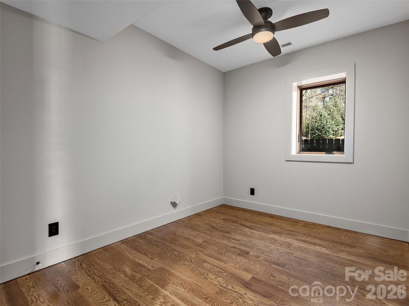Lower-level third bedroom or office/study featuring oak hardwood floors, ceiling fan, and a flexible layout for guests, work, or hobbies.