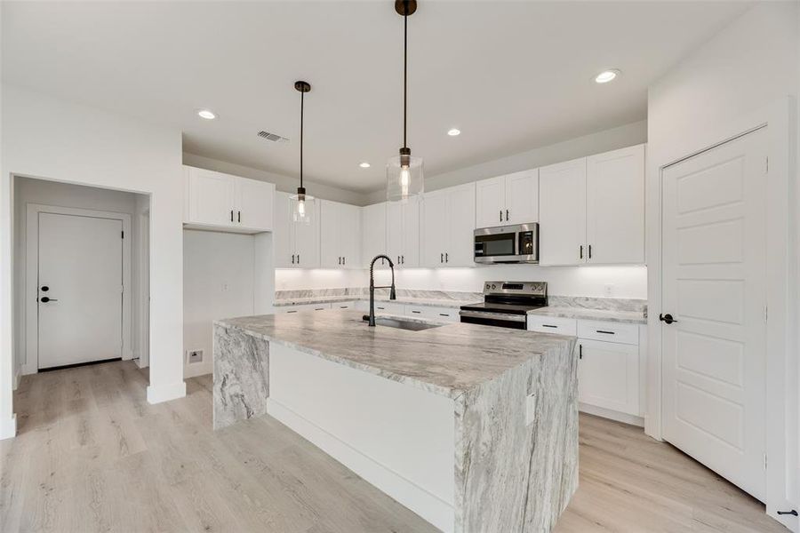 Kitchen featuring light stone countertops, appliances with stainless steel finishes, an island with sink, pendant lighting, and recessed lighting