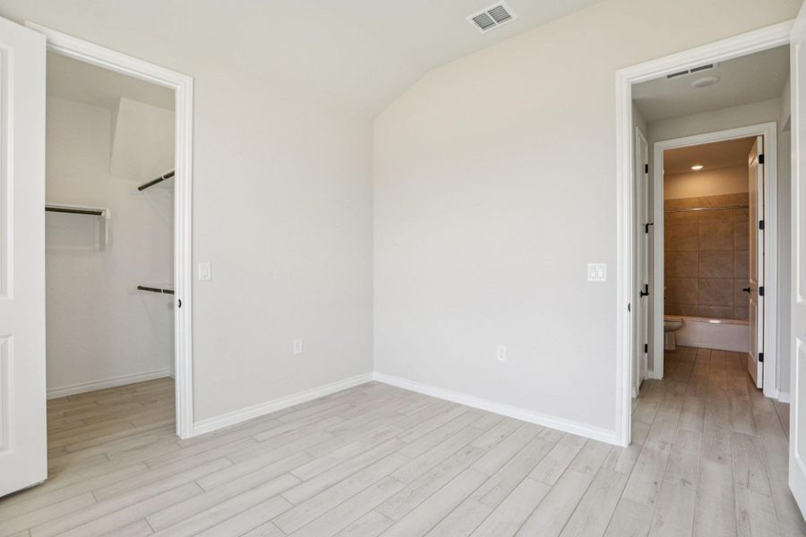Unfurnished bedroom featuring a walk in closet, light wood-style flooring, and ensuite bath