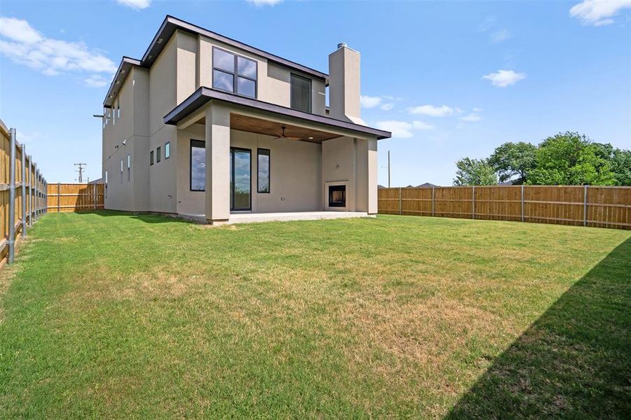 The property features a spacious backyard with a lawn, a covered patio, and a built-in outdoor fireplace The property features a spacious backyard with a lawn, a covered patio, and a built-in outdoor fireplace