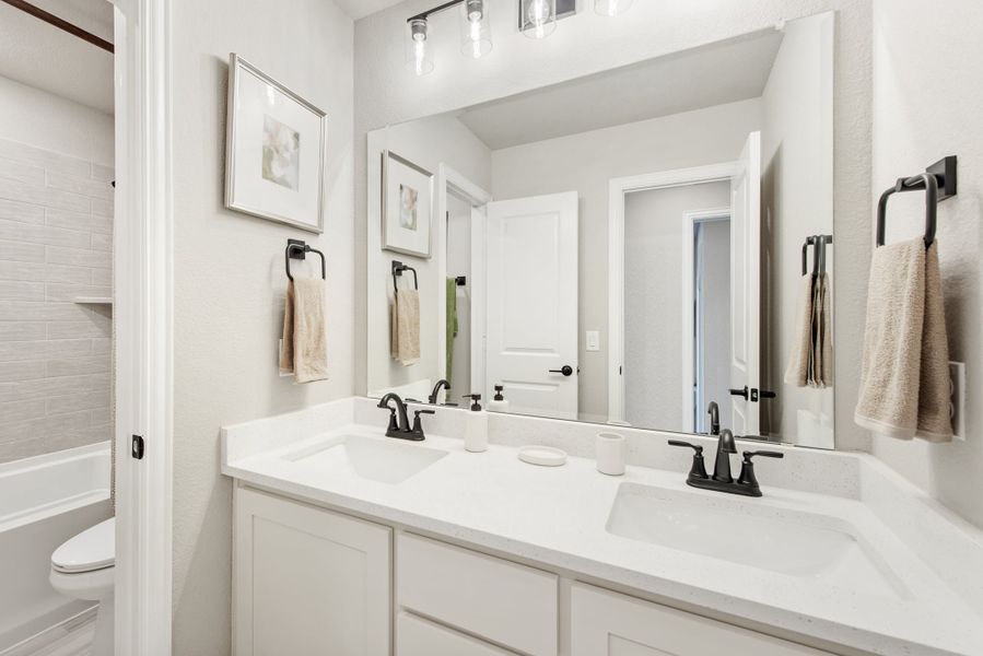 Bathroom with double sink vanity, white quartz countertop, black faucets, and large mirror above
