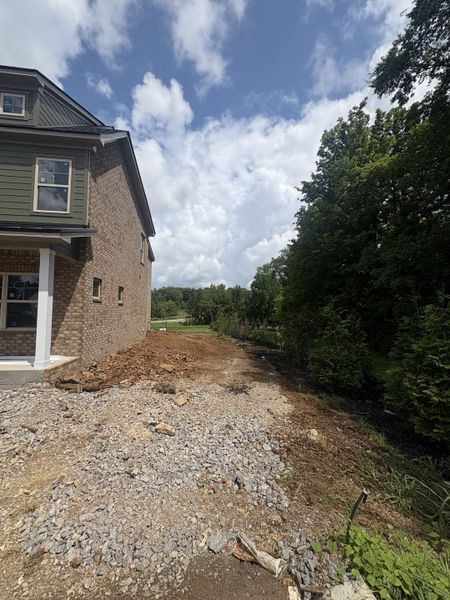 As of July 8, 2026, the current progress is as pictured. The house is situated on a corner lot, surrounded by lush greenery and a tree line.
