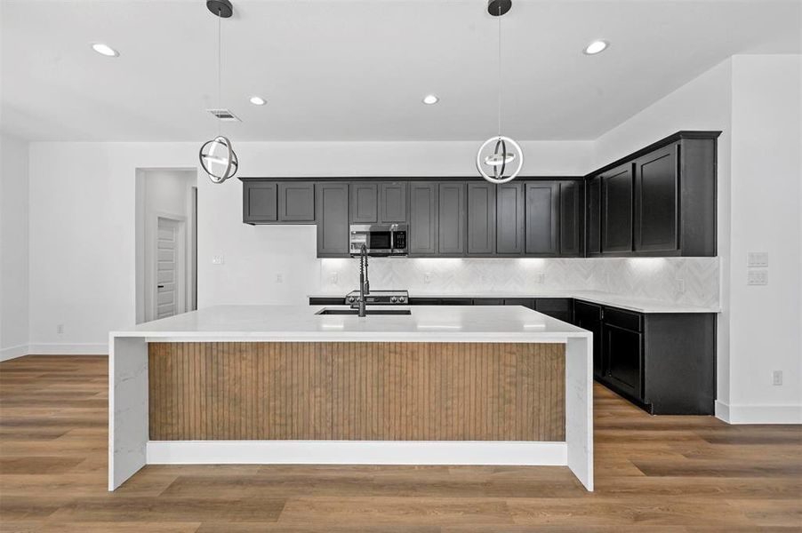 Kitchen with a center island with sink, light hardwood / wood-style flooring, and pendant lighting