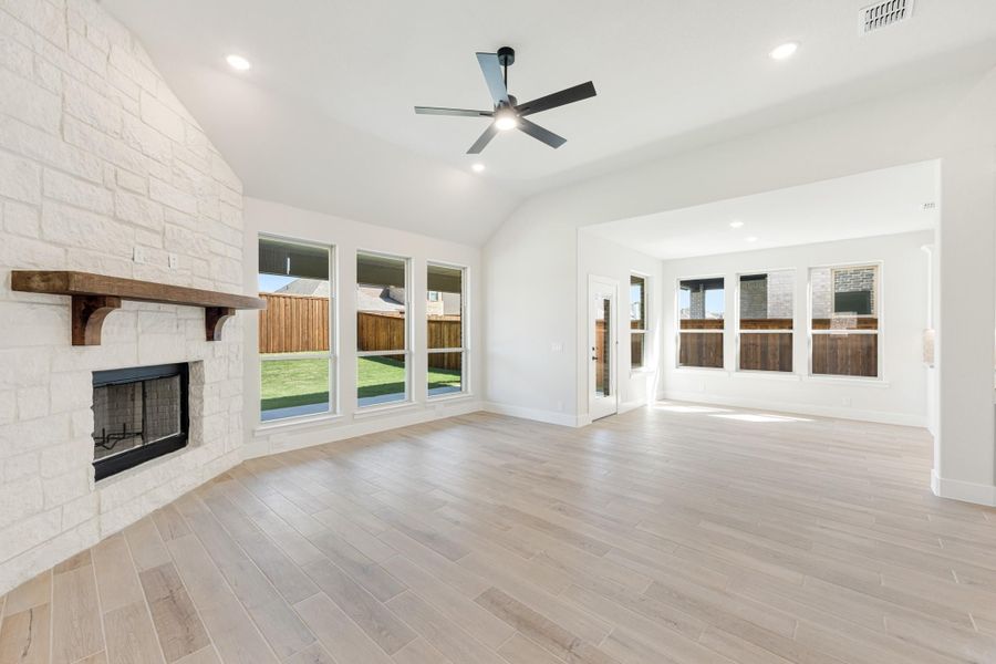 Open living room with stone fireplace, wood mantel, ceiling fan, and light hardwood floors