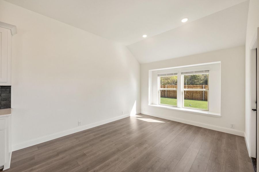 Empty room with vaulted ceiling, hardwood floors, and large window overlooking backyard Empty room with vaulted ceiling, hardwood floors, and large window overlooking backyard