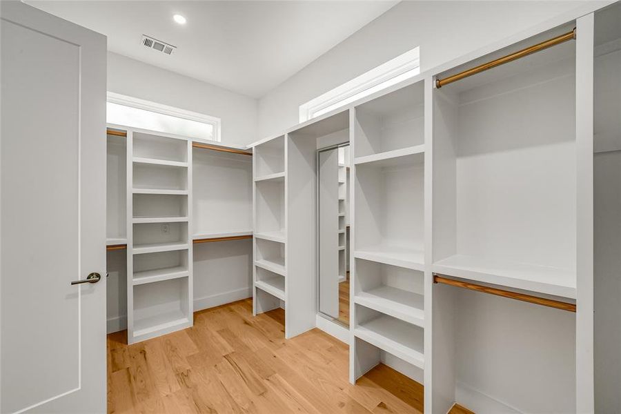 Walk-in closet featuring built-in white shelving, hanging rods, and wood-finish flooring