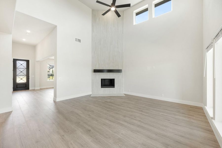 Open living room with high ceilings, floor-to-ceiling tile fireplace, ceiling fan, and light wood floors