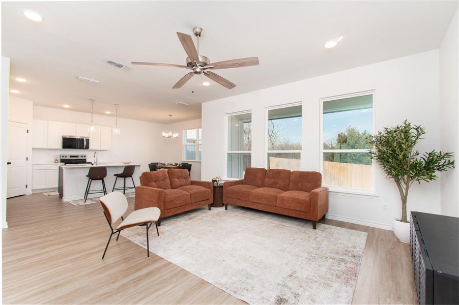 Living room featuring light wood-style flooring, ceiling fan, and hanging lights