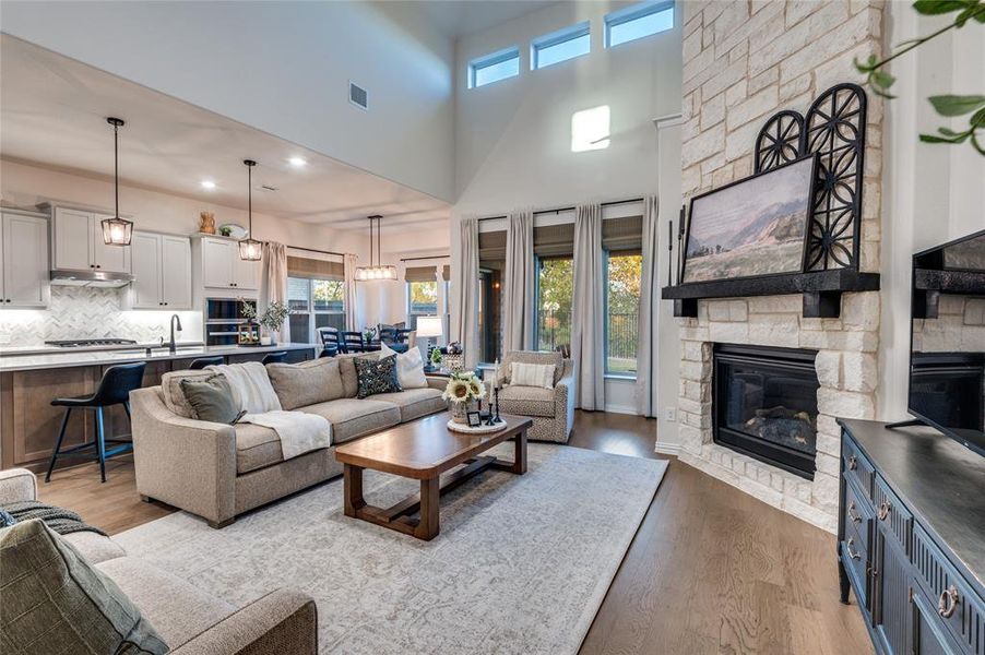 Living room featuring plenty of natural light, wood finished floors, a towering ceiling, a stone fireplace, and recessed lighting