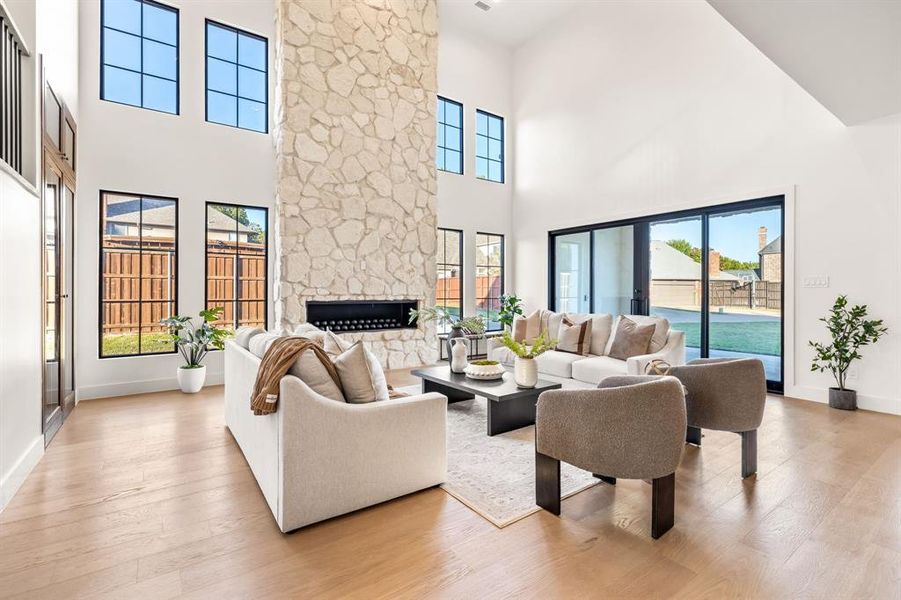 Living area featuring a stone fireplace, light wood finished floors, plenty of natural light, and a towering ceiling Living area featuring a stone fireplace, light wood finished floors, plenty of natural light, and a towering ceiling