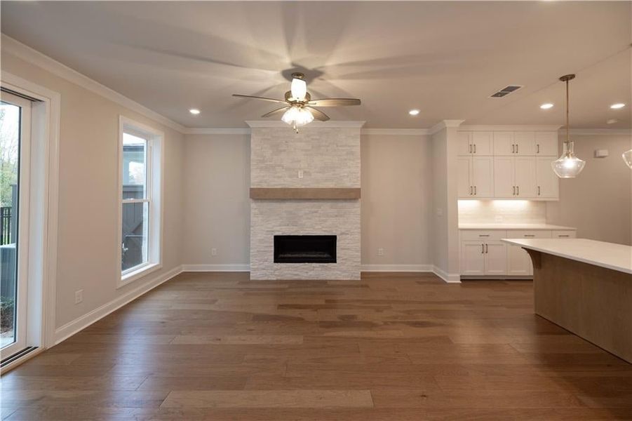 Unfurnished living room with ornamental molding, dark wood finished floors, a stone fireplace, ceiling fan, and recessed lighting